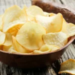Crispy golden cassava chips served in a rustic wooden bowl next to raw manioc root tubers